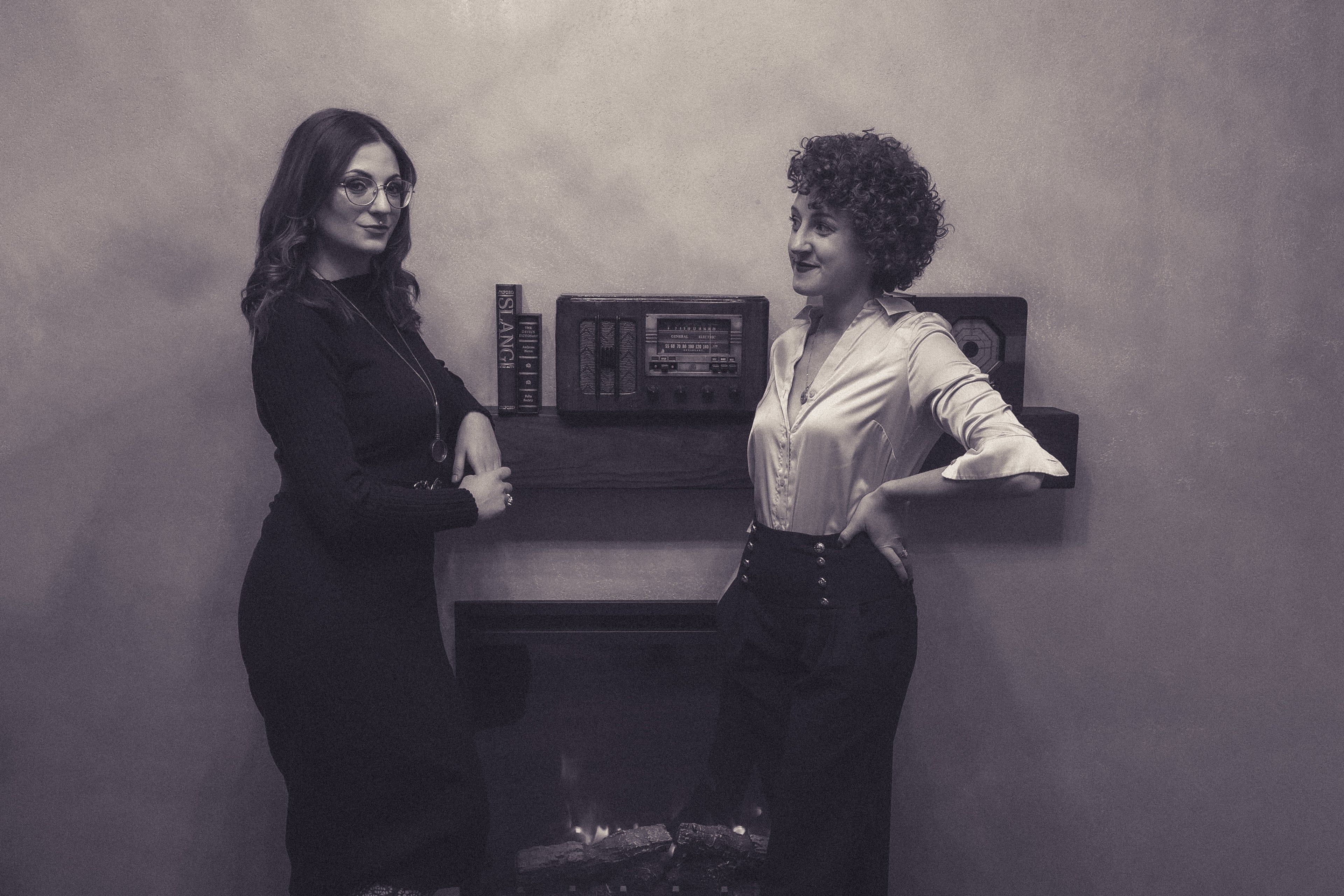Black and white photo of Charlotte and Dina in front of a fireplace with old radio. 